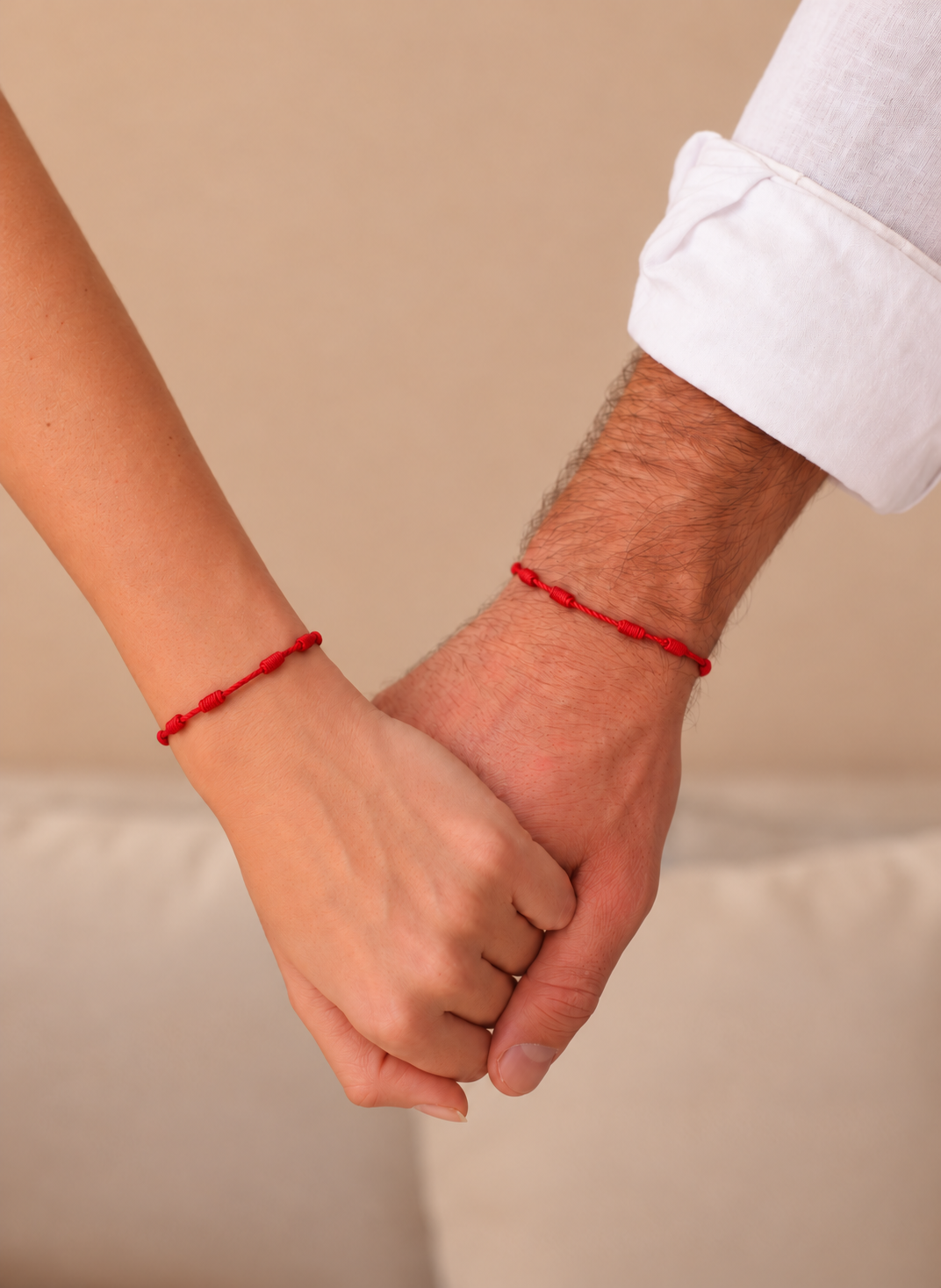 Dos personas de la mano con pulseras de hilo rojo