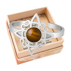 Anillo abierto de acero plateado con diseño de Nudo de Bruja y piedra central de Ojo de Tigre marrón con destellos dorados.