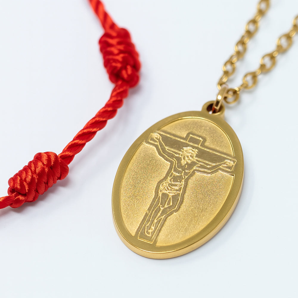 Detalle de medalla dorada de Jesús crucificado con cordón rojo