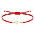 Pulsera de hilo rojo liso con una Cruz de Santiago central en acero dorado, decorada con esferas metálicas doradas y cierre ajustable de nudo corredizo.
