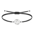 Pulsera de hilo encerado negro ajustable con pieza central circular de acero inoxidable plateado, presentando la silueta calada de la Virgen de Candelaria.