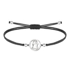Pulsera de hilo encerado negro ajustable con pieza central circular de acero inoxidable plateado, presentando la silueta calada de la Virgen de Candelaria.