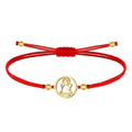 Pulsera de hilo encerado rojo ajustable con medalla central circular de acero inoxidable dorado, mostrando la silueta calada de la Virgen de Candelaria. Detalles de bolitas doradas en los extremos.