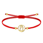 Pulsera de hilo encerado rojo ajustable con medalla central circular de acero inoxidable dorado, mostrando la silueta calada de la Virgen de Candelaria. Detalles de bolitas doradas en los extremos.