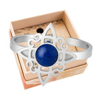 Anillo abierto de acero plateado con diseño de Nudo de Bruja y piedra central de Lapislázuli azul con destellos dorados.