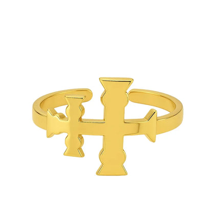 Anillo de acero inoxidable dorado con la Cruz de Caravaca en posición horizontal, diseño abierto y ajustable sobre fondo de pergamino