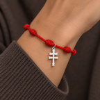 Pulsera roja de nudos con Cruz de Caravaca plateada en la muñeca. Escena ilustrativa generada con IA.
