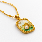 Collar dorado con medallón rectangular claro y verde, detalle en una mesa blanca