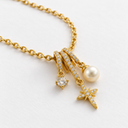 Collar dorado con piedra redonda, estrella y perla, detalle en una mesa blanca