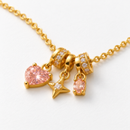 Collar dorado con corazón rosa, estrella y piedra ovalada, detalle en una mesa blanca