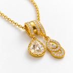 Collar dorado con colgante de gota y doble aro, detalle en una mesa blanca