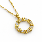 Collar de círculo dorado con circonitas, detalle sobre una superficie blanca.