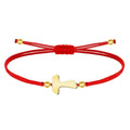 Pulsera de hilo rojo liso con cruz Tau central en acero dorado, esferas decorativas doradas y cierre ajustable.