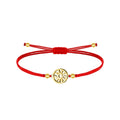 Pulsera de cordón rojo con cierre corredizo, motivo circular calado de Eguzkilore y cuatro cuentas de color dorado sobre fondo blanco