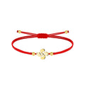 Pulsera de doble cordón rojo con cierre corredizo, cuatro cuentas doradas y conector central Lauburu dorado de cuatro brazos curvos sobre fondo blanco